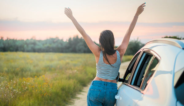 woman on the road feeling ecstatic with her car spring cleaning her up on the air and basking in the sun