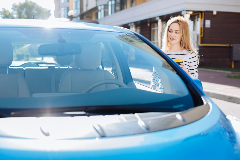 A blue car that a blonde woman in a stripe shirt looking at selling her car. 