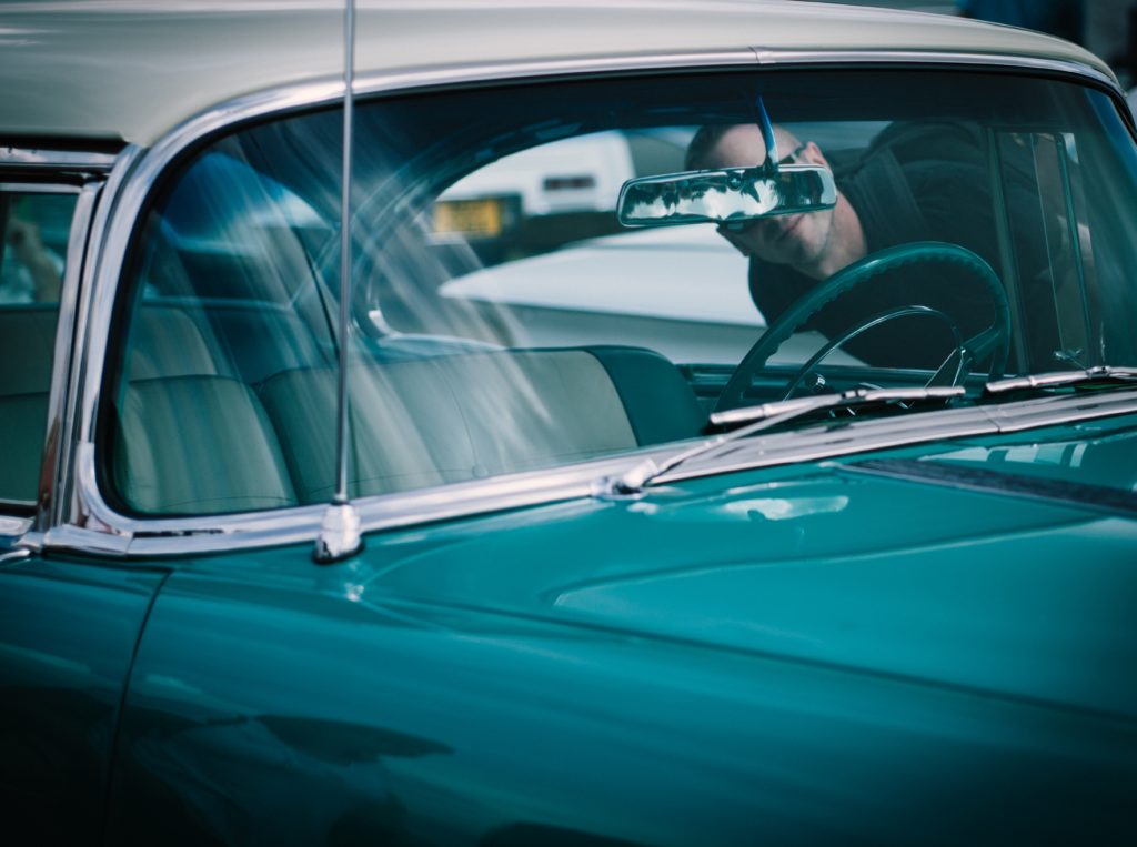 man looking inside a shiny vintage car  trying to think what best price on a car he can offer.