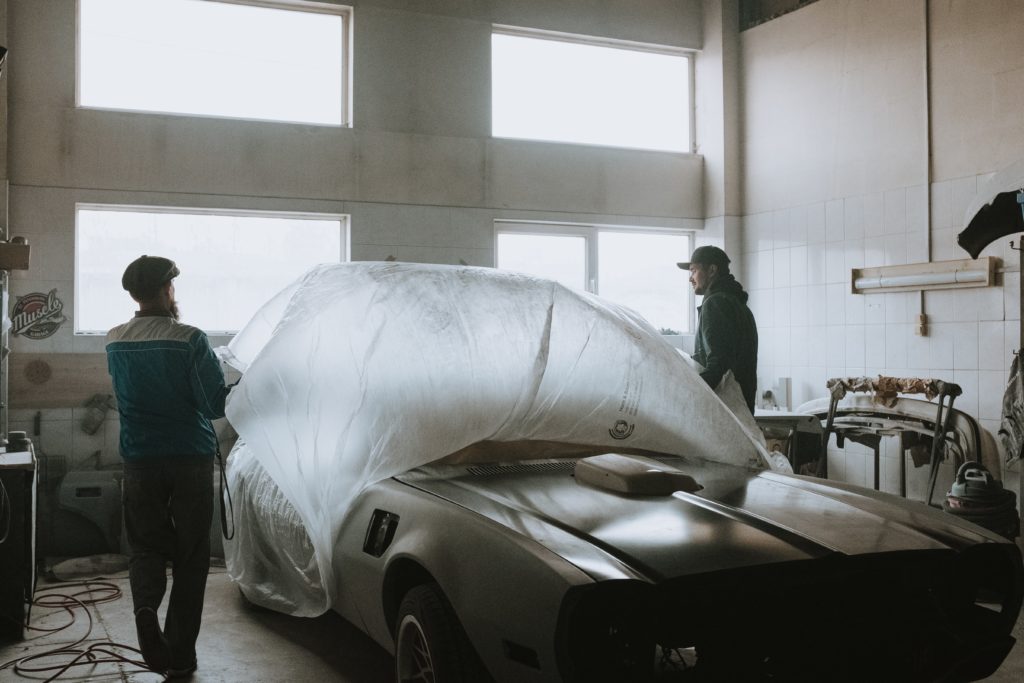 Two men working in a car shop taking off a car cover from a vintage car 