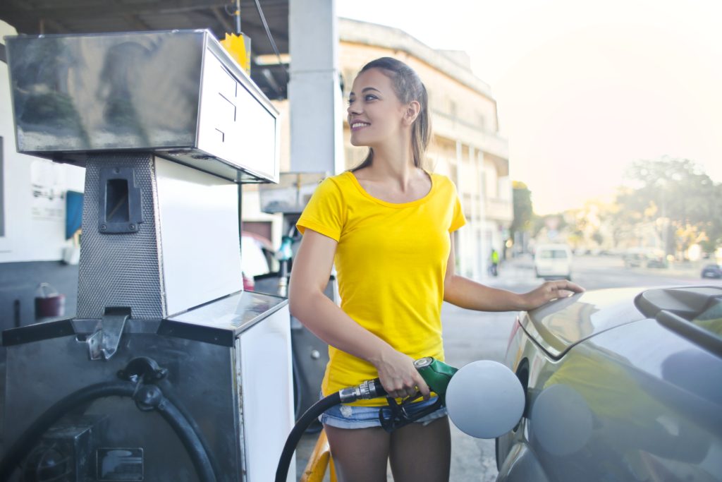 A girl in a yellow shirt putting gas on her car and trying to save money on gas