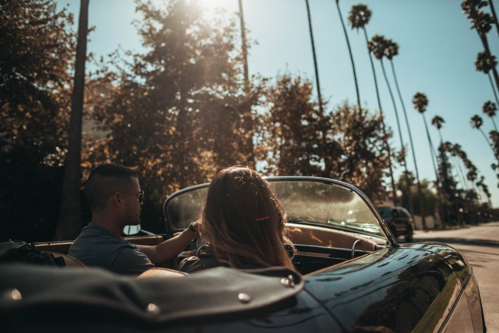 Man and woman driving a convertible under a sunny weather 